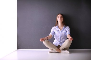 Genç bir kadın yerde, kara duvarın yanında oturuyor.