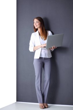 Bir dizüstü bilgisayar, gri arka plan üzerinde ayakta tutan genç kadın