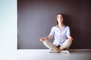 Genç bir kadın yerde, kara duvarın yanında oturuyor.