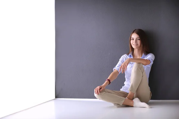 Молодая женщина сидит на полу рядом с темной стеной — стоковое фото