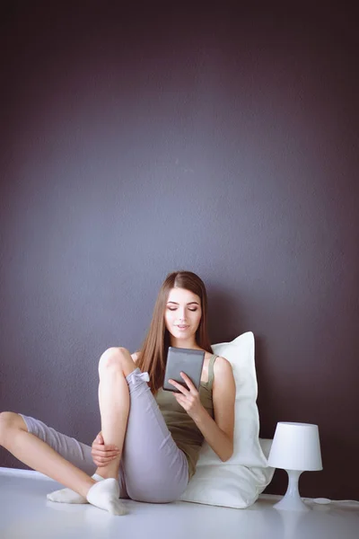 Hezká brunetka ženu sedící na podlaze s polštářem a letadlo tabulka — Stock fotografie