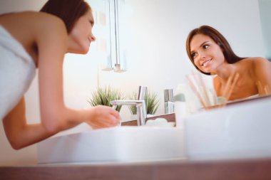 Genç bir kadın banyoda yüzünü temiz suyla yıkıyor.