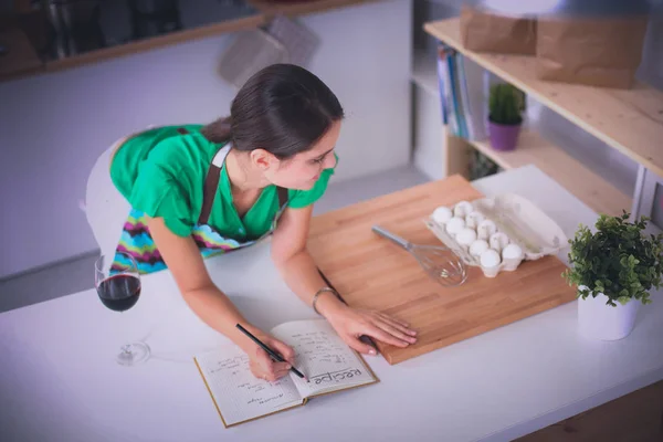 Gelukkig mooie vrouw permanent in haar keuken schrijven op een laptop thuis — Stockfoto