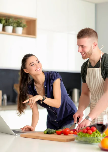 Jongeman snijden groenten en vrouw staan met laptop in de keuken — Stockfoto