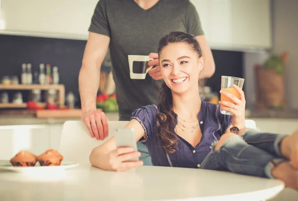 Pareja feliz usando smartphone sentado en la cocina —  Fotos de Stock