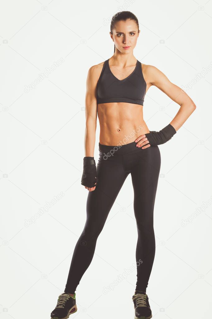 Muscular young woman posing in sportswear against black background.