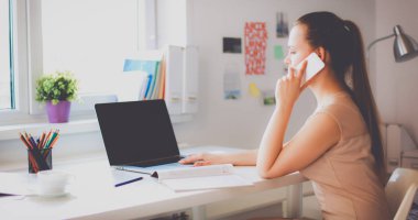 Genç iş kadını masada oturuyor ve telefonla konuşuyor.