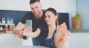 Mutlu çift mutfakta oturmuş smartphone kullanarak