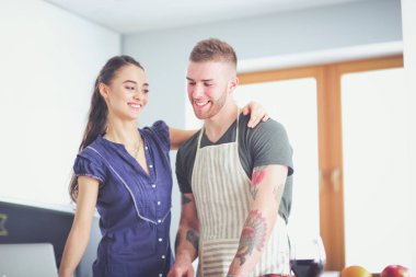 Sebze doğrayan genç bir adam ve mutfakta dizüstü bilgisayarı olan bir kadın.