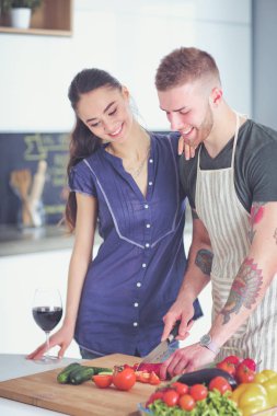 Sebze doğrayan genç bir adam ve mutfakta dizüstü bilgisayarı olan bir kadın.