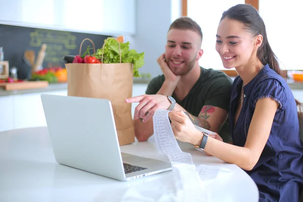 Pareja pagando sus cuentas con el ordenador portátil en la cocina en casa — Foto de Stock