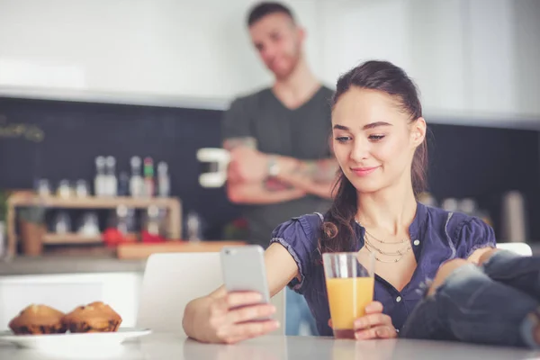 Pareja feliz usando smartphone sentado en la cocina —  Fotos de Stock