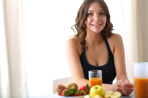 Flicka sitter i köket på skrivbord med frukt och glas med juice — Stockfoto