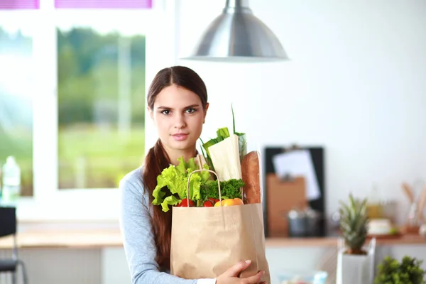 Femeie tânără care deține sac de cumpărături alimentar cu legume. Stând în bucătărie — Fotografie, imagine de stoc