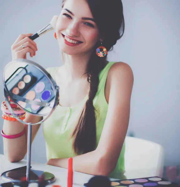 Joven hermosa mujer haciendo maquillaje cerca del espejo, sentado en el escritorio — Foto de Stock