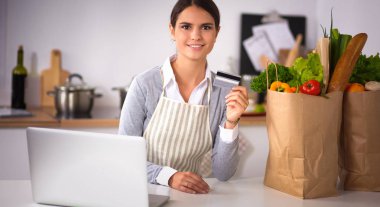Mutfakta bilgisayar ve kredi kartı kullanan gülümseyen bir kadın.