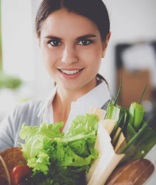 Ung kvinna som håller i matkassen med grönsaker Står i köket. — Stockfoto