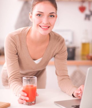 mutfağında suyu yudumlarken bir dizüstü bilgisayar kullanan kadın