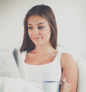 Genç ve güzel kadın yatakta gazete okuyan ve bir fincan çay keyfi