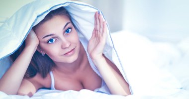 Genç ve güzel bir kadın örtülü olarak yatakta yatıyor.