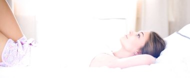 Güzel genç bir kadın, rahat ve mutlu bir şekilde yatakta uzanıyor.