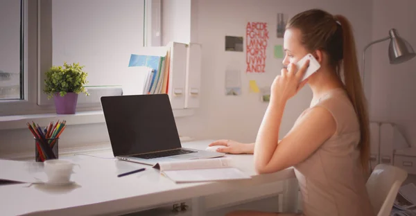 Jovem empresária sentada na mesa e conversando ao telefone — Fotografia de Stock