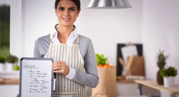 Mujer en la cocina en casa, de pie cerca de escritorio con carpeta —  Fotos de Stock