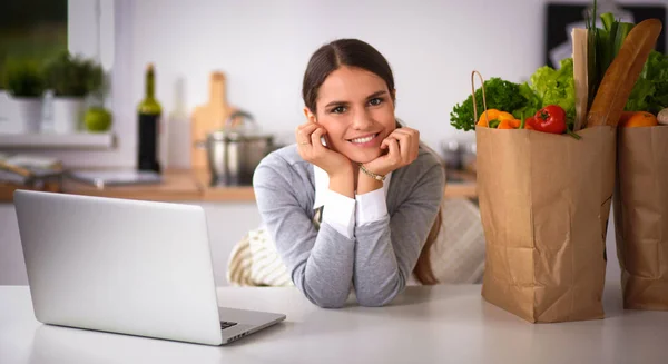 Schöne junge Frau kocht mit Blick auf Laptop-Bildschirm mit Quittung in der Küche — Stockfoto