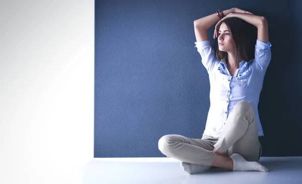 Young woman sitting on the floor near dark wall — Stock Photo, Image