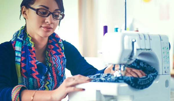 Junge Frau näht, während sie am Arbeitsplatz sitzt — Stockfoto