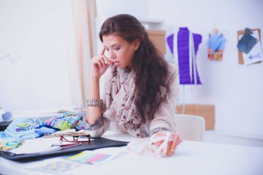 Gülümseyen kadın moda tasarımcısı ofis masasında oturuyor.