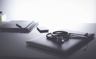 Dizüstü bilgisayarı, steteskopu ve defteri olan bir doktorun çalışma yeri.