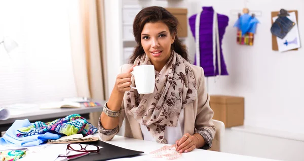 Junge Designerin sitzt auf dem Schreibtisch mit Tasse — Stockfoto