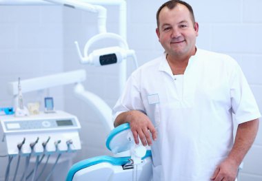 Diş kliniğinde duran gülümseyen bir dişçinin portresi.