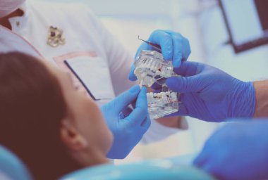 Diş muayenehanesinde kıdemli erkek dişçi kadın hastayla konuşuyor ve tedaviye hazırlanıyor.