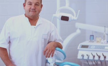 Diş kliniğinde duran gülümseyen bir dişçinin portresi.