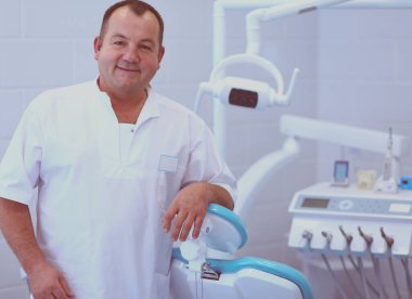 Diş kliniğinde duran gülümseyen bir dişçinin portresi.