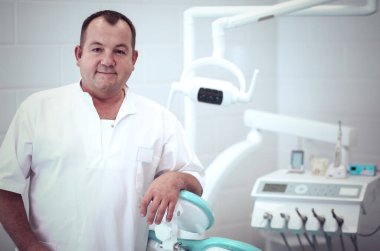 Diş kliniğinde duran gülümseyen bir dişçinin portresi.