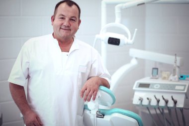 Diş kliniğinde duran gülümseyen bir dişçinin portresi.