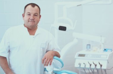 Diş kliniğinde duran gülümseyen bir dişçinin portresi.