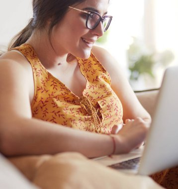 Evde dizüstü bilgisayar üzerinde çalışan kanepede oturan genç kadın