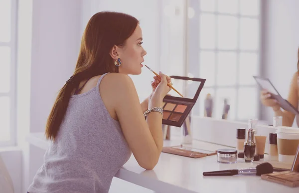 Mujer morena aplicando maquillaje para una cita nocturna frente a un espejo — Foto de Stock