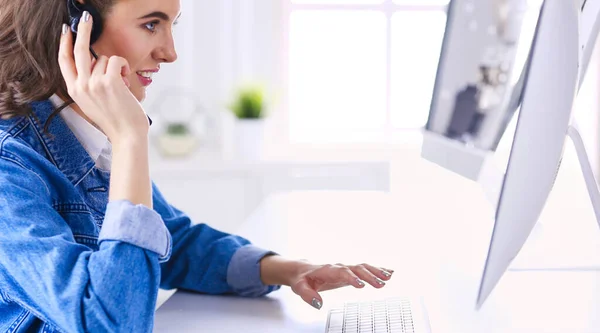 Felice affascinante giovane donna seduta e lavorare con il computer portatile utilizzando cuffie in ufficio — Foto Stock