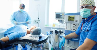 Ameliyat odasında arka planda erkek cerrah var.