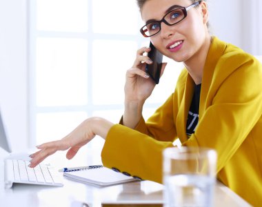 İş kadını ofiste bilgisayar ve cep telefonu kullanarak işine konsantre oluyor.