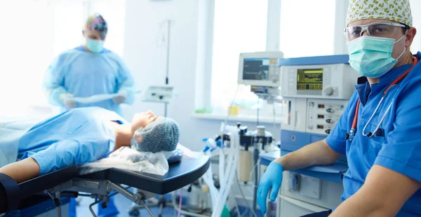 Ameliyat odasında arka planda erkek cerrah var.