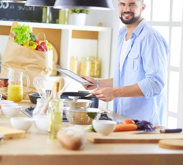 Man following recipe on digital tablet and cooking tasty and healthy food in kitchen at home