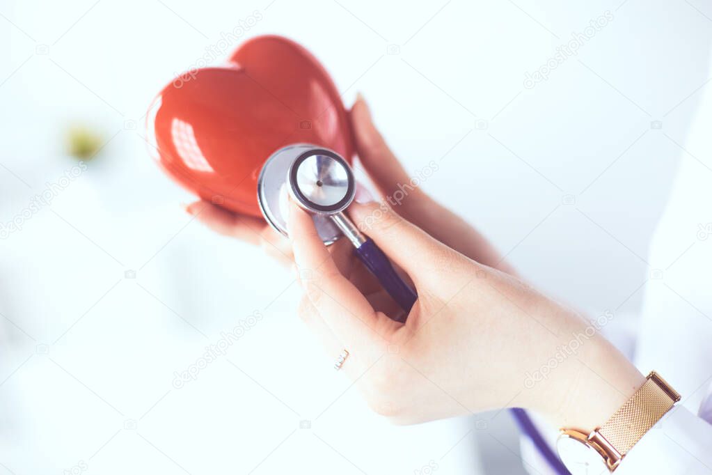 A doctor with stethoscope examining red heart, isolated on white background