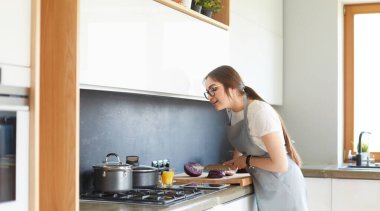 Mutfakta yemek yapmak için tablet bilgisayar kullanan genç bir kadın.