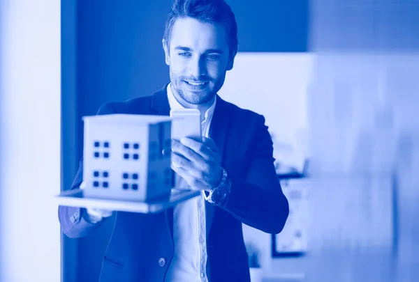 Businessman holding house miniature on hand standing in office.